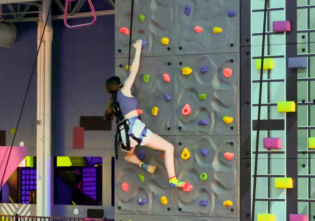 A participant scales a climbing wall inside Urban Air Adventure Park